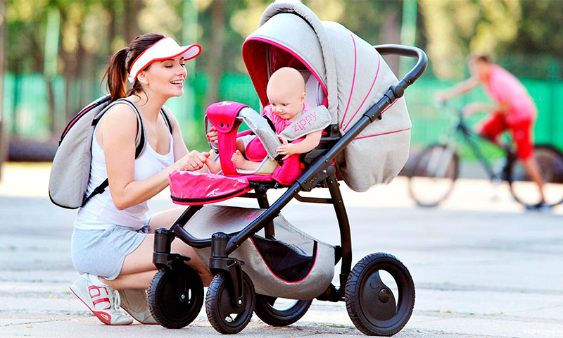 улыбчивая мама сидит рядом с малышом в коляске на улице